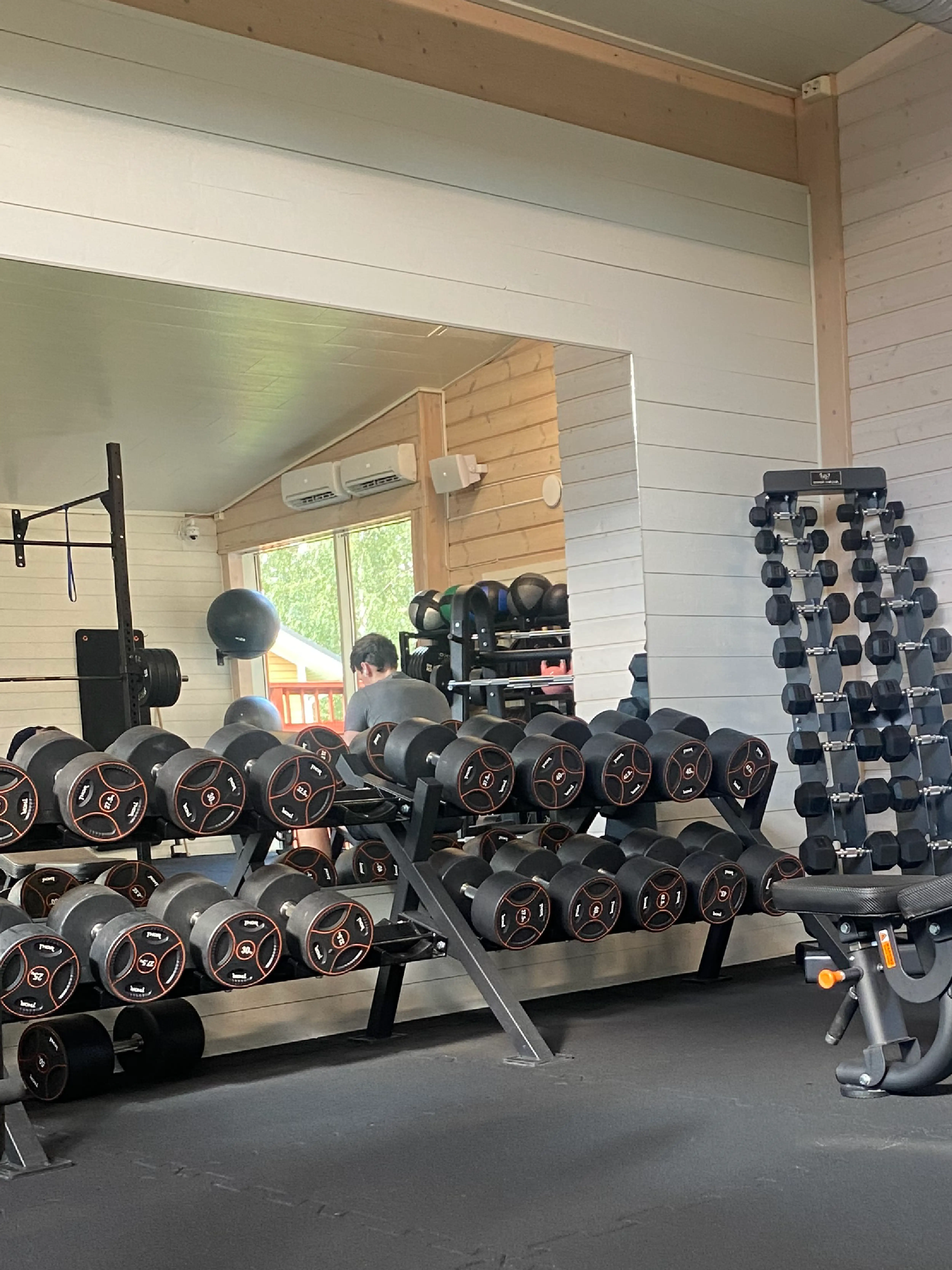 Hantelställ med spegel bakom i ett välutrustat gym på Hälsofabriken, med flera par hantlar i olika viktklasser.