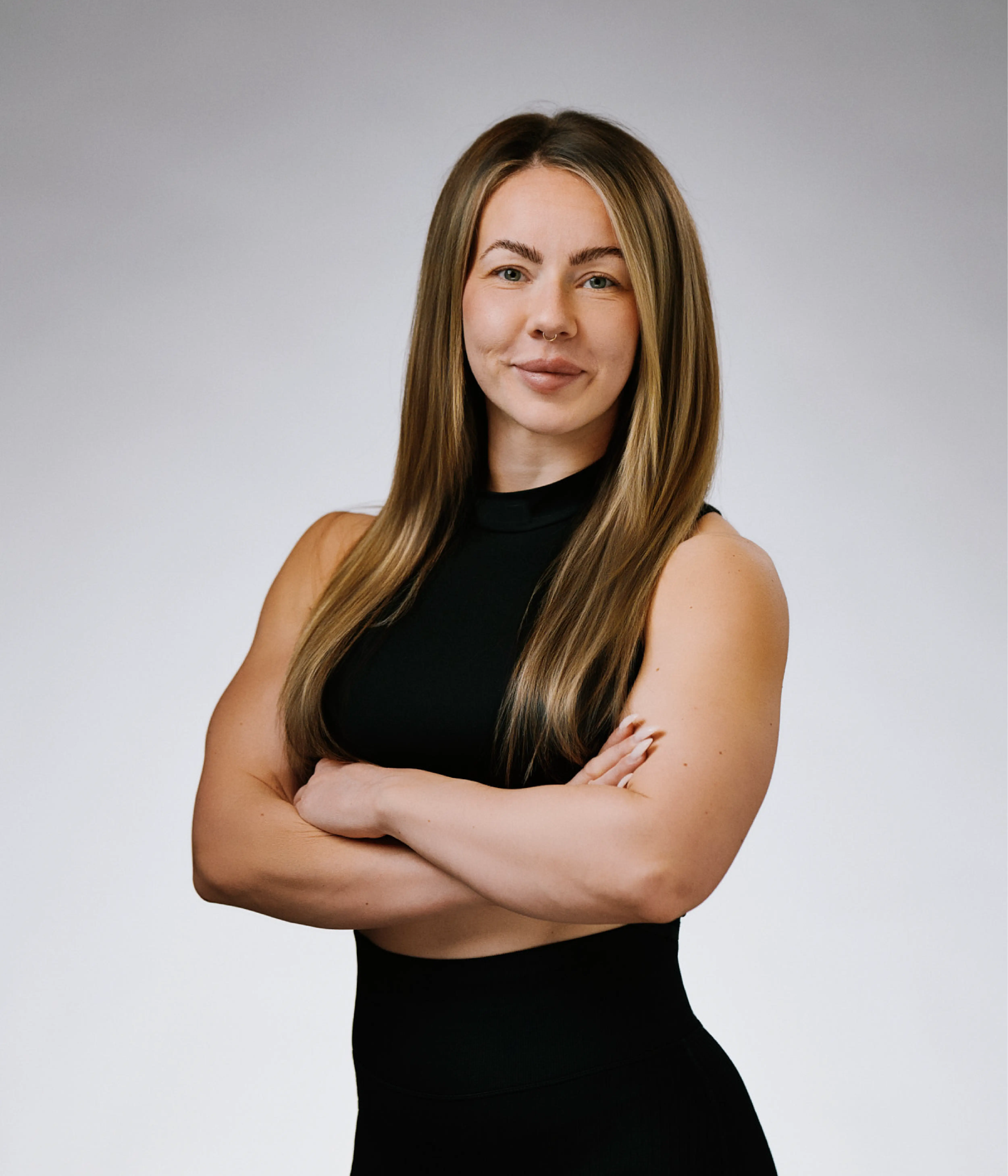 Porträtt av Elin Liewendahl, personlig tränare på Hälsofabriken. Hon står med armarna i kors, bär svart träningskläder och har långt, rakt hår. Bakgrunden är ljus och neutral.